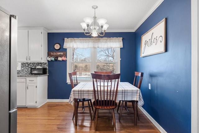 dining room with ornamental molding, a notable chandelier, and light hardwood / wood-style flooring