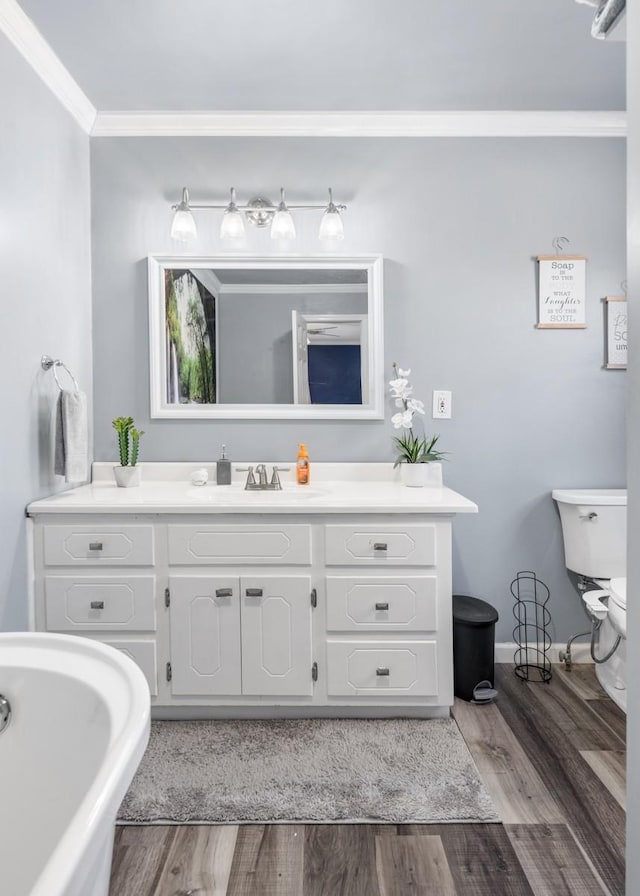 bathroom featuring crown molding, hardwood / wood-style floors, vanity, a tub to relax in, and toilet