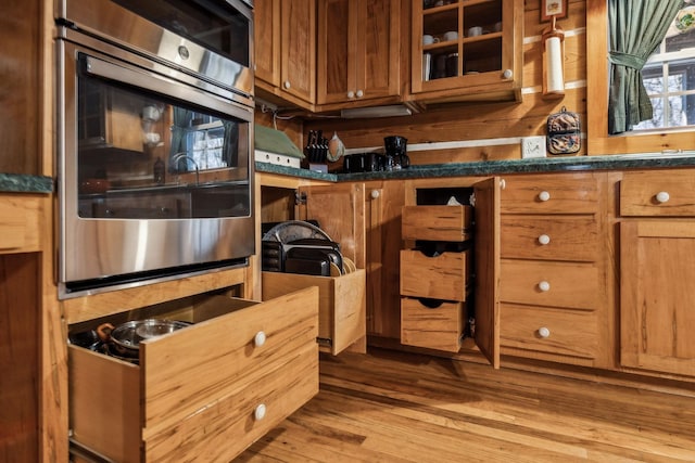 kitchen featuring stainless steel oven, dark stone counters, and light hardwood / wood-style flooring