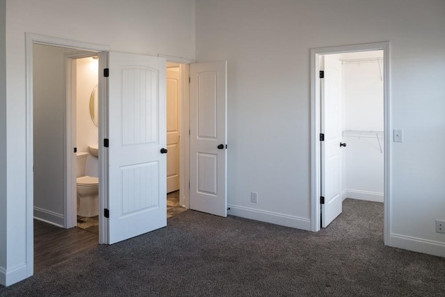 unfurnished bedroom with a closet, a walk in closet, dark carpet, and ensuite bath