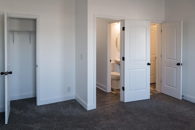 unfurnished bedroom with dark colored carpet, a spacious closet, ensuite bathroom, and a closet