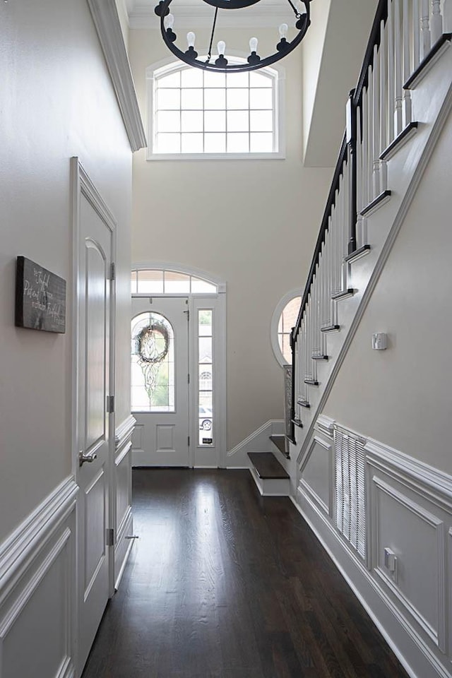 entryway featuring dark wood-type flooring, ornamental molding, an inviting chandelier, and a high ceiling