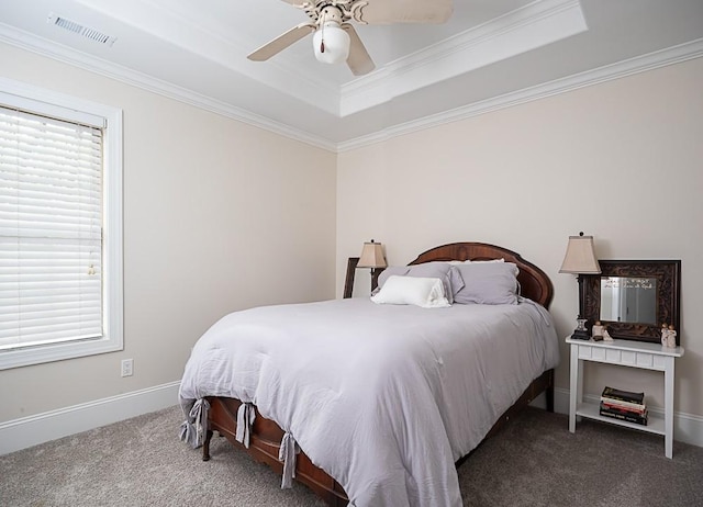 carpeted bedroom with multiple windows, a tray ceiling, ornamental molding, and ceiling fan