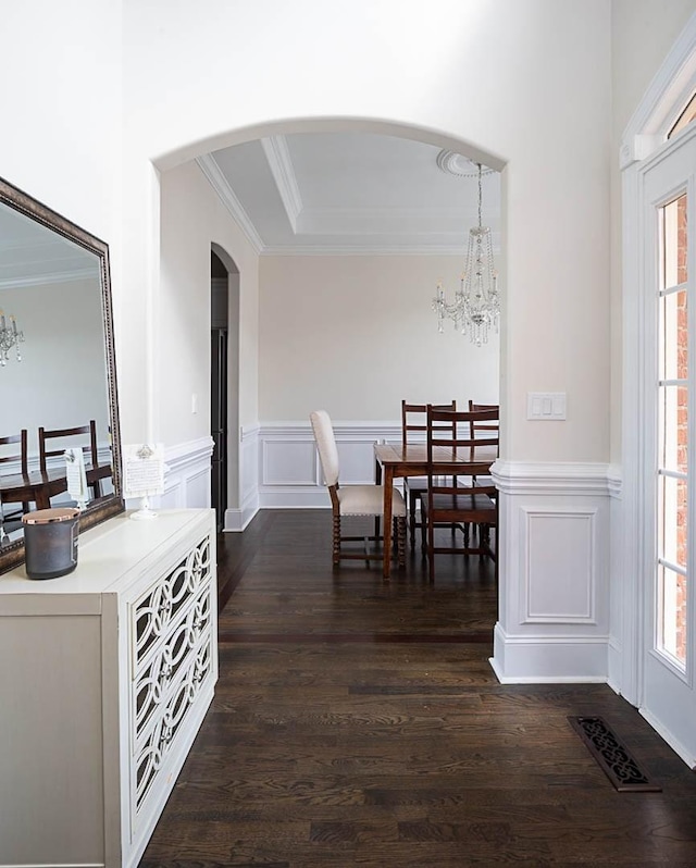 dining area featuring dark wood-type flooring, ornamental molding, a chandelier, and a healthy amount of sunlight