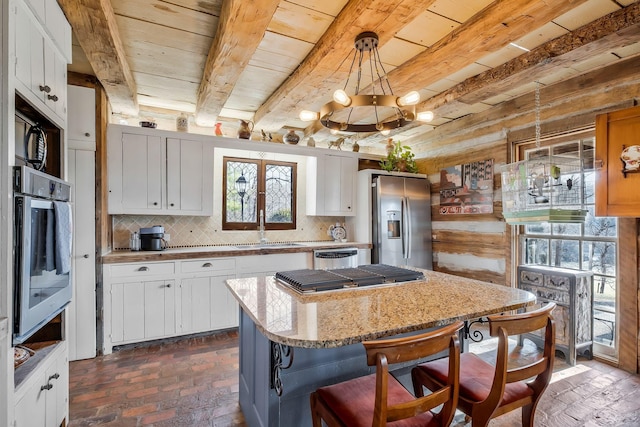 kitchen featuring pendant lighting, white cabinets, stainless steel appliances, and beamed ceiling