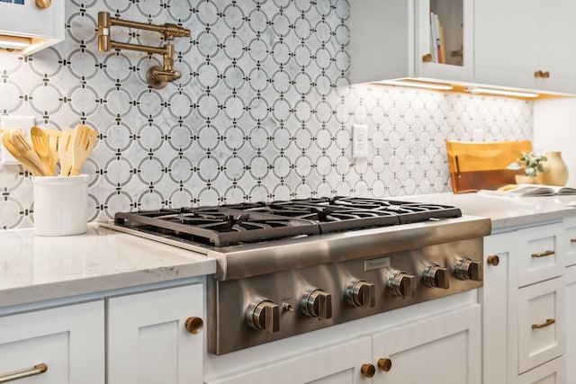 kitchen with white cabinetry, backsplash, light stone countertops, and stainless steel gas stovetop