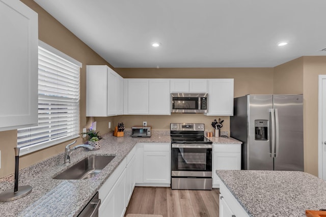 kitchen featuring stainless steel appliances, white cabinetry, sink, and light stone counters