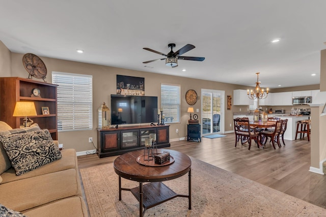 living room featuring ceiling fan with notable chandelier and light hardwood / wood-style flooring