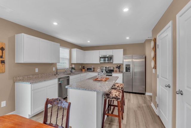 kitchen featuring a kitchen breakfast bar, a kitchen island, stainless steel appliances, light hardwood / wood-style floors, and white cabinets