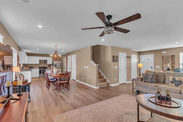 living room with ceiling fan with notable chandelier and light wood-type flooring