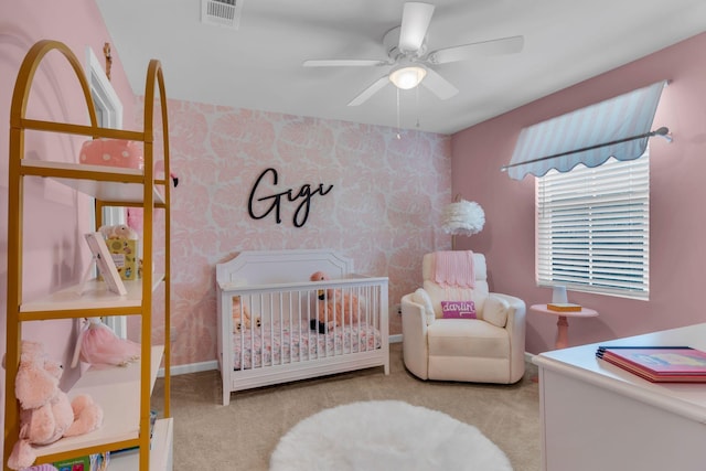 bedroom featuring a nursery area, ceiling fan, and light carpet