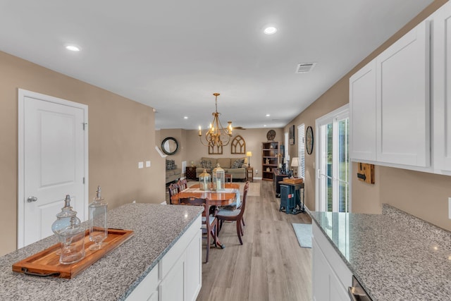 kitchen with an inviting chandelier, white cabinetry, light stone counters, and light hardwood / wood-style floors