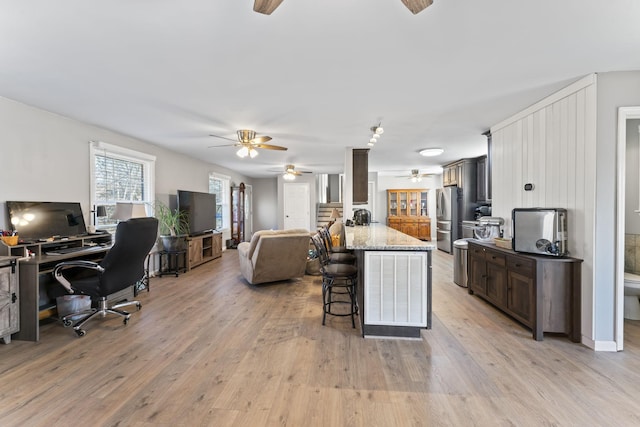 kitchen with light hardwood / wood-style flooring, stainless steel fridge, dark brown cabinetry, and a breakfast bar