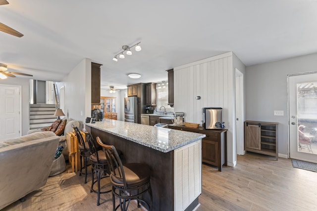 kitchen featuring light hardwood / wood-style flooring, kitchen peninsula, ceiling fan, stainless steel appliances, and light stone countertops