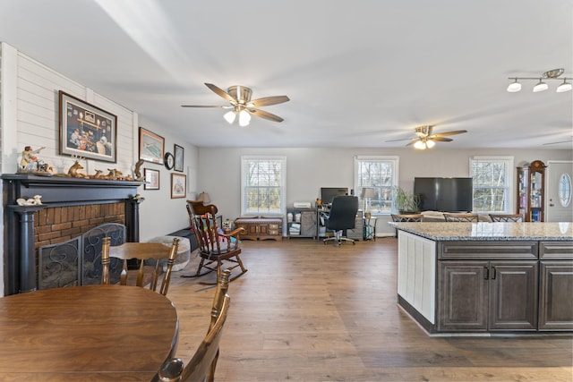 kitchen with dark hardwood / wood-style floors, dark brown cabinets, light stone counters, a brick fireplace, and a healthy amount of sunlight