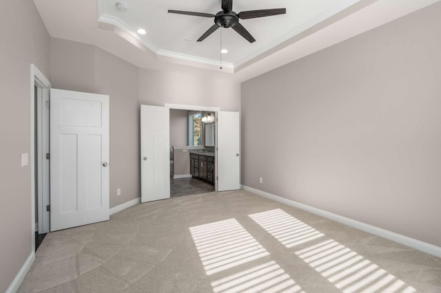 unfurnished bedroom featuring a tray ceiling, ensuite bath, light colored carpet, and ceiling fan