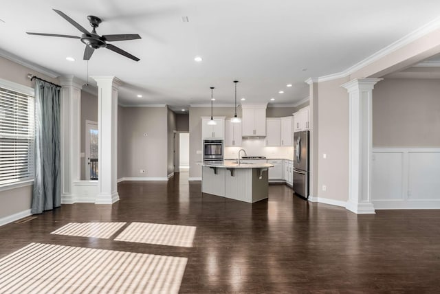 kitchen featuring pendant lighting, decorative columns, an island with sink, white cabinets, and ornamental molding