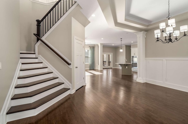 interior space with a chandelier, ornamental molding, a tray ceiling, hardwood / wood-style floors, and decorative columns