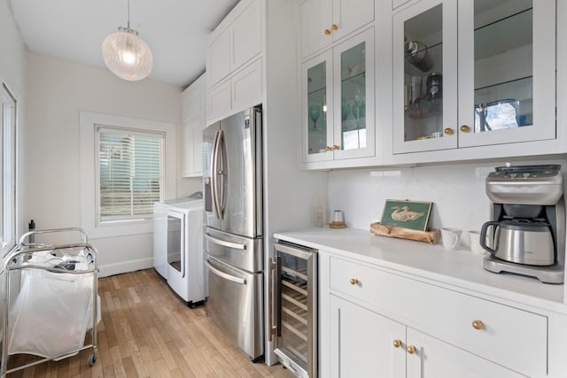 kitchen with white cabinetry, decorative light fixtures, stainless steel fridge with ice dispenser, beverage cooler, and washer and clothes dryer