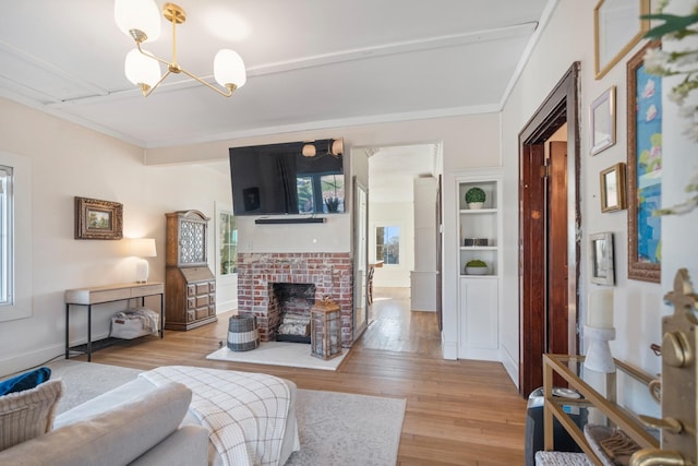 living room with ornamental molding, light hardwood / wood-style floors, a brick fireplace, an inviting chandelier, and built in shelves