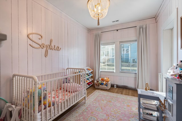 bedroom featuring hardwood / wood-style flooring, a nursery area, wooden walls, and a chandelier