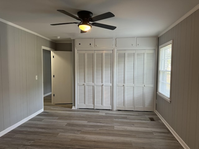 unfurnished bedroom featuring ceiling fan, ornamental molding, light hardwood / wood-style flooring, and two closets