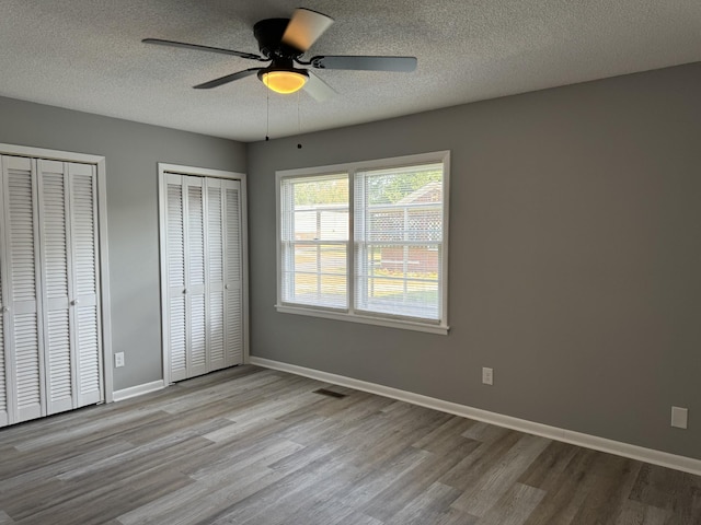 unfurnished bedroom featuring multiple closets, ceiling fan, a textured ceiling, and light hardwood / wood-style flooring