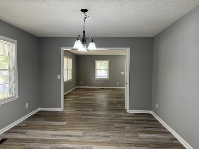 unfurnished dining area with hardwood / wood-style floors, a chandelier, and a textured ceiling