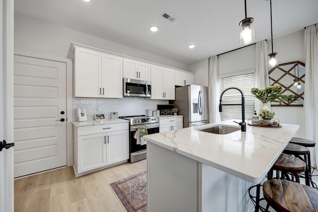 kitchen with white cabinetry, sink, hanging light fixtures, a kitchen island with sink, and stainless steel appliances