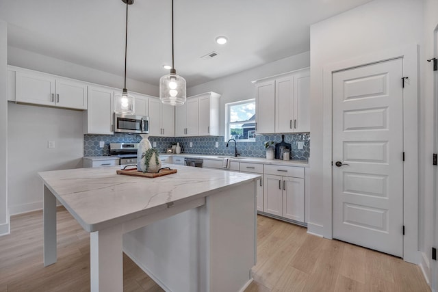 kitchen featuring appliances with stainless steel finishes, white cabinetry, hanging light fixtures, light stone counters, and a kitchen island