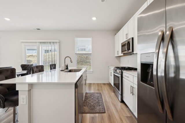 kitchen featuring sink, white cabinets, a kitchen island with sink, stainless steel appliances, and light wood-type flooring