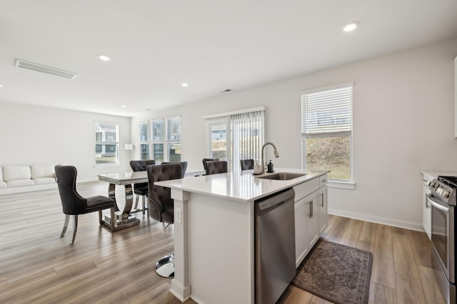 kitchen with sink, a kitchen island with sink, stainless steel appliances, light hardwood / wood-style floors, and white cabinets