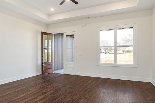 unfurnished room featuring a tray ceiling, ceiling fan, and dark wood-type flooring