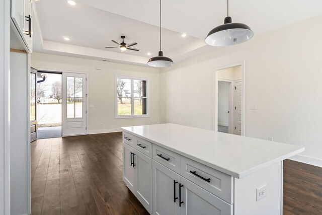 kitchen with a center island, white cabinetry, a tray ceiling, dark hardwood / wood-style floors, and decorative light fixtures