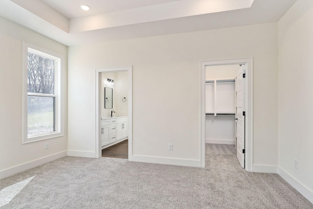 unfurnished bedroom with sink, a spacious closet, connected bathroom, a raised ceiling, and light colored carpet