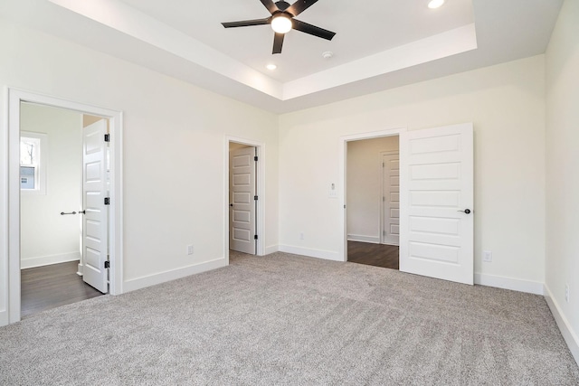 unfurnished bedroom with dark colored carpet, connected bathroom, and a raised ceiling