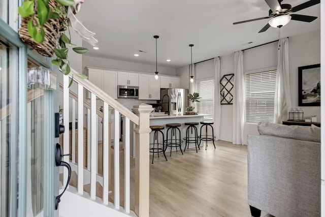 interior space with appliances with stainless steel finishes, hanging light fixtures, a kitchen bar, white cabinets, and a center island with sink