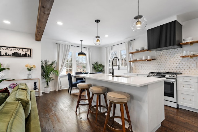 kitchen featuring sink, stainless steel gas range, white cabinetry, ventilation hood, and an island with sink