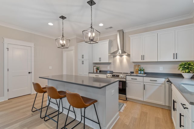 kitchen with pendant lighting, wall chimney range hood, appliances with stainless steel finishes, a center island, and white cabinets