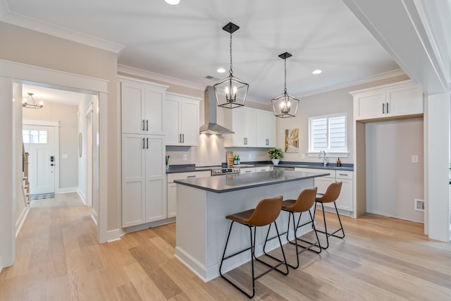 kitchen featuring a kitchen island, decorative light fixtures, white cabinets, crown molding, and wall chimney range hood