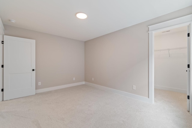 unfurnished bedroom with a spacious closet, light carpet, and a closet