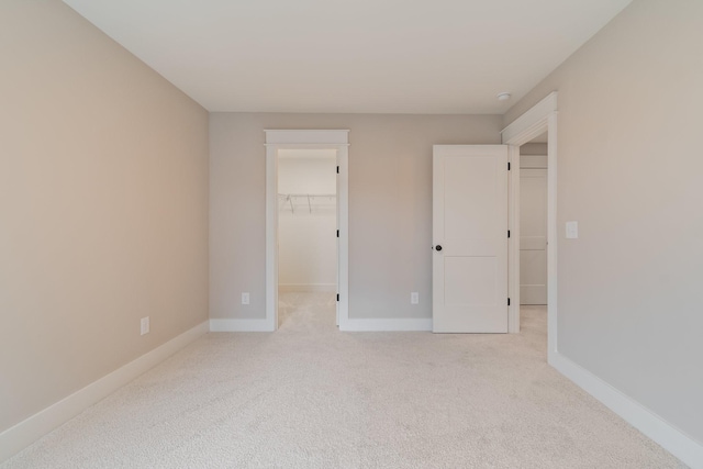 unfurnished bedroom with a walk in closet, light colored carpet, and a closet