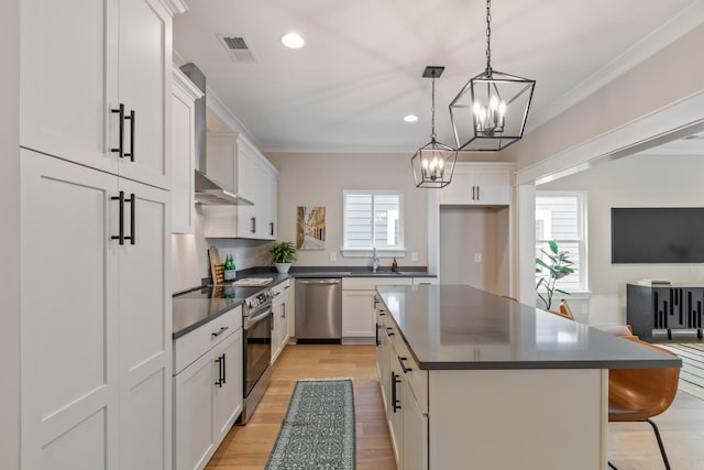 kitchen featuring appliances with stainless steel finishes, white cabinetry, hanging light fixtures, a center island, and wall chimney exhaust hood