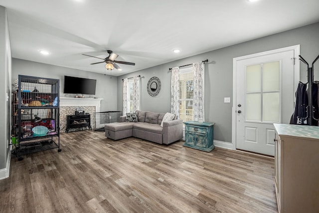 living room featuring a tile fireplace, ceiling fan, and light wood-type flooring