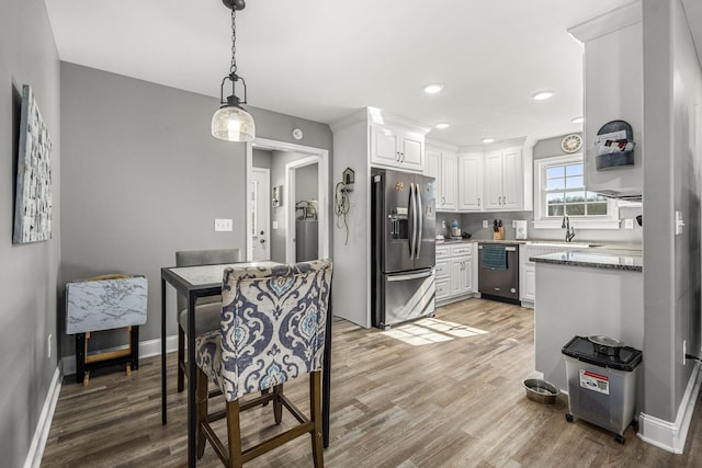 kitchen with sink, light stone counters, appliances with stainless steel finishes, hardwood / wood-style floors, and white cabinets