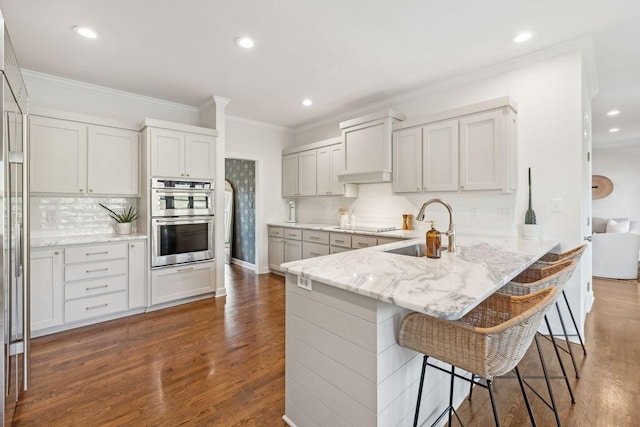 kitchen with a breakfast bar, sink, kitchen peninsula, double oven, and white cabinets