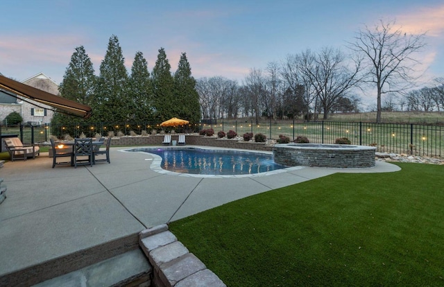 pool at dusk with a patio area and a lawn