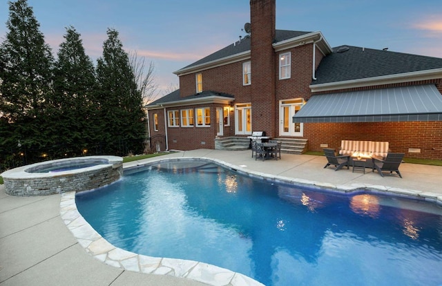 pool at dusk featuring area for grilling, a fire pit, a patio, and an in ground hot tub