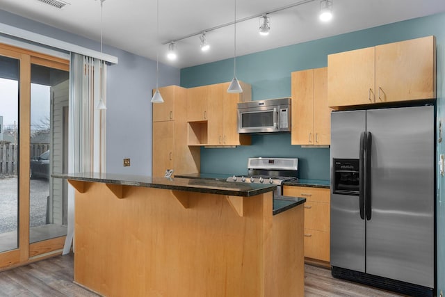 kitchen featuring pendant lighting, stainless steel appliances, wood-type flooring, a center island with sink, and light brown cabinets