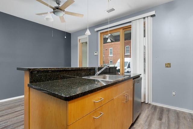 kitchen featuring dishwasher, sink, dark stone countertops, dark wood-type flooring, and a center island with sink